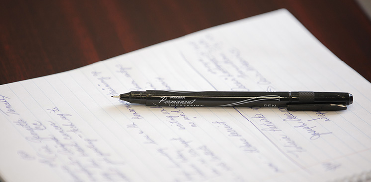 A SKILCRAFT permanent pen sits on top of a spiral bound notebook with notes written on the page.