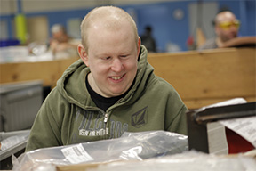 A man smiles at the camera while sitting at his work station.