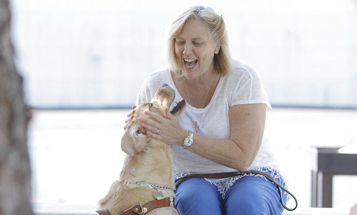 A woman laughs and pets her guide dog while sitting on a bench outside of IFB Solutions in Winston-Salem.