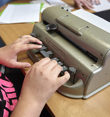 A woman learns how to type braille using a brailler.