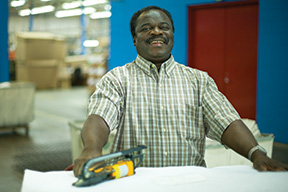 A man smiles at the camera while working on a mattress.
