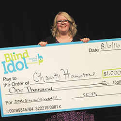 A young woman smiles while holding a giant check from the Blind Idol competition.