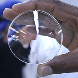 A hand holds a lens used in eye glasses.
