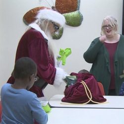 Santa pulls a gift from his bag as a boy and a woman watch