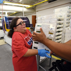 Winter, a worker in the optical lab, hands off trays to another worker