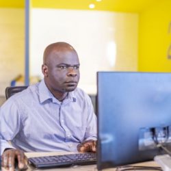 man sits at desk facing computer monitor