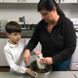 Woman helping kid mix ingredients in a kitchen.