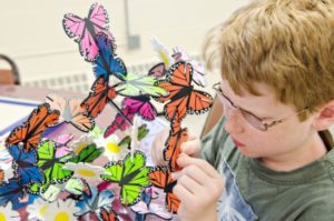 A SEE camper builds a sculpture from wooden butterflies