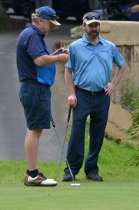 Grant standing with a golf club speaking to another golfer