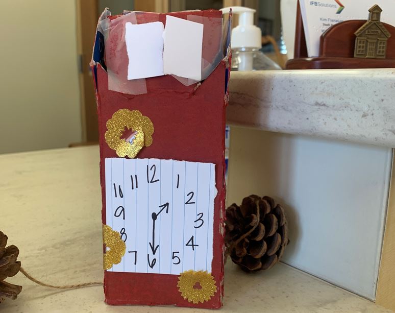red coocoo clock with index card shutters and clock face, twine and pine cone winding chain, and tactile stickers to represent wood carvings