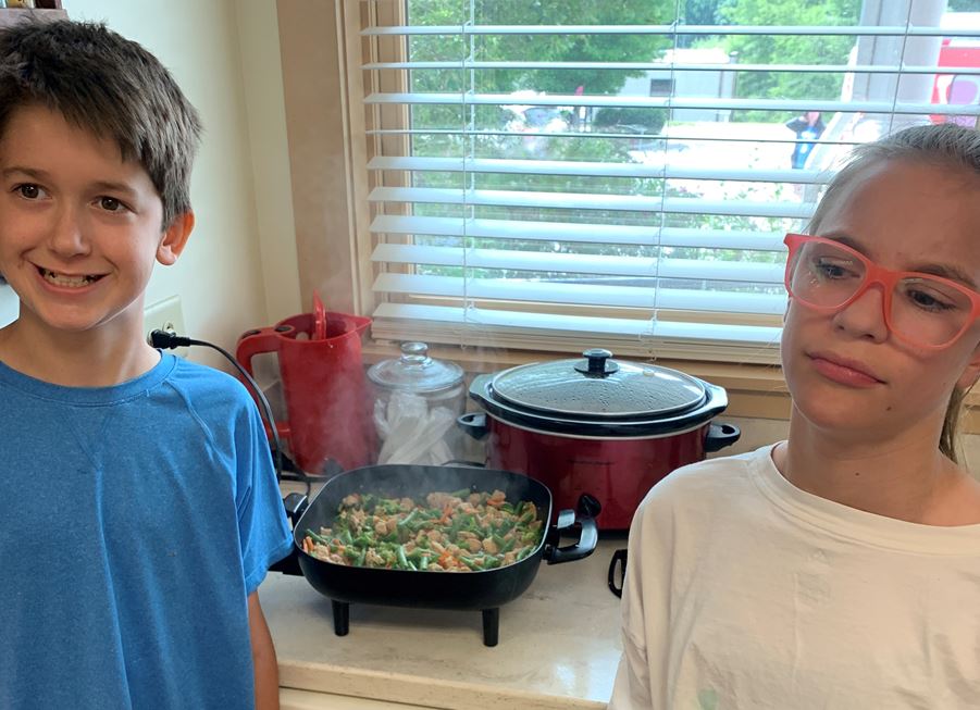 Tanner and Molly standing in front of electric frying pans of stir fry.