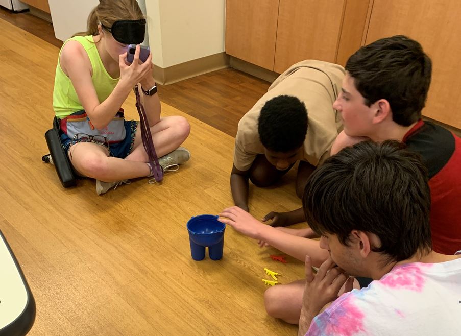 campers playing a game on the floor aiming plastic ants at a plastic pair of pants with suspenders