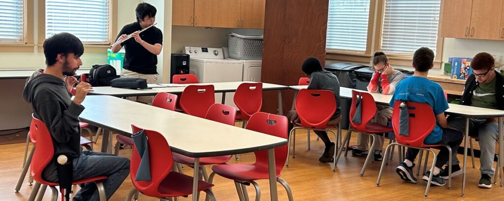 young man playing the flute in the schoolhouse kitchen for the S.E.E. kids