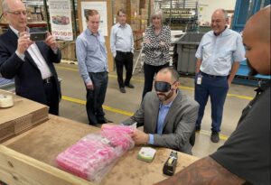 Members of the AbilityOne Commission look on as a sighted person attempts packaging while blindfolded