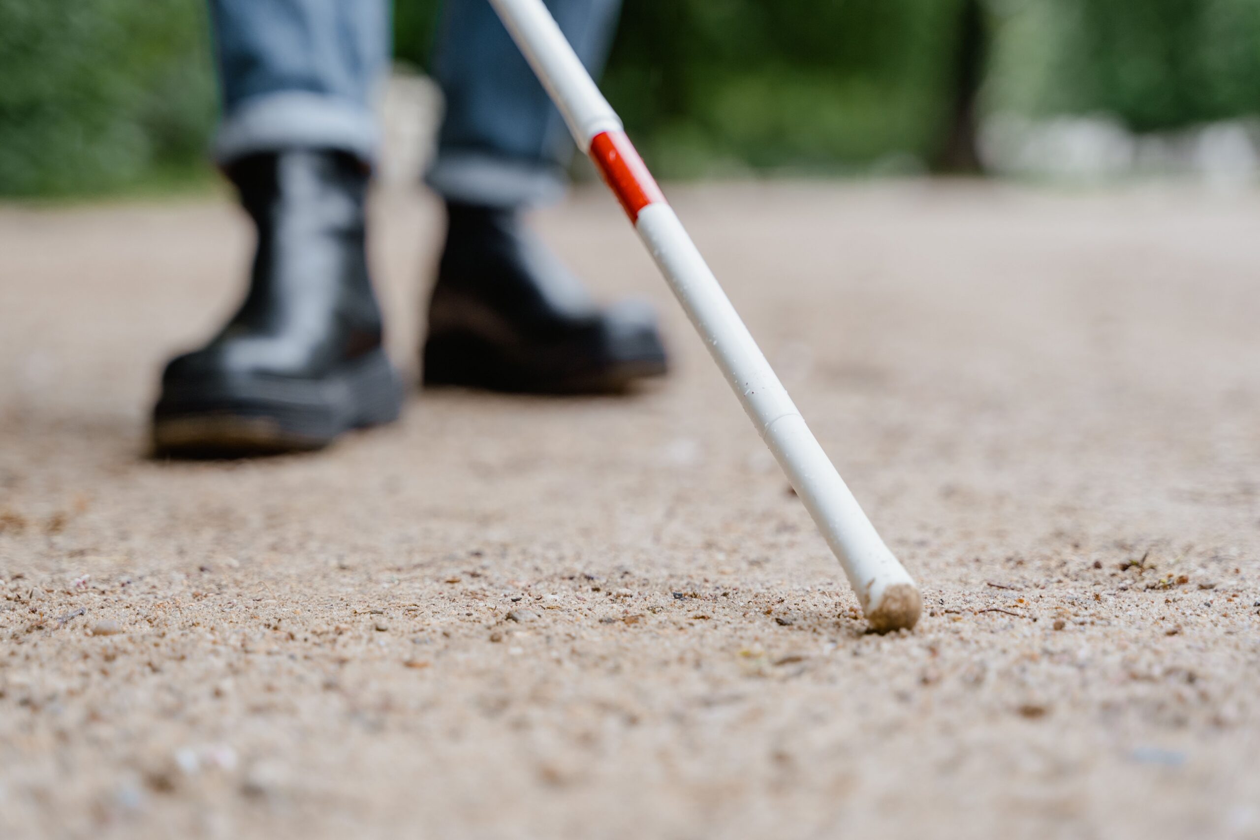 A person's black boots and end of their white cane.